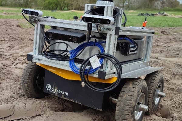 Ein kleiner Feldroboter mit Sensorsystem steht auf einem Acker