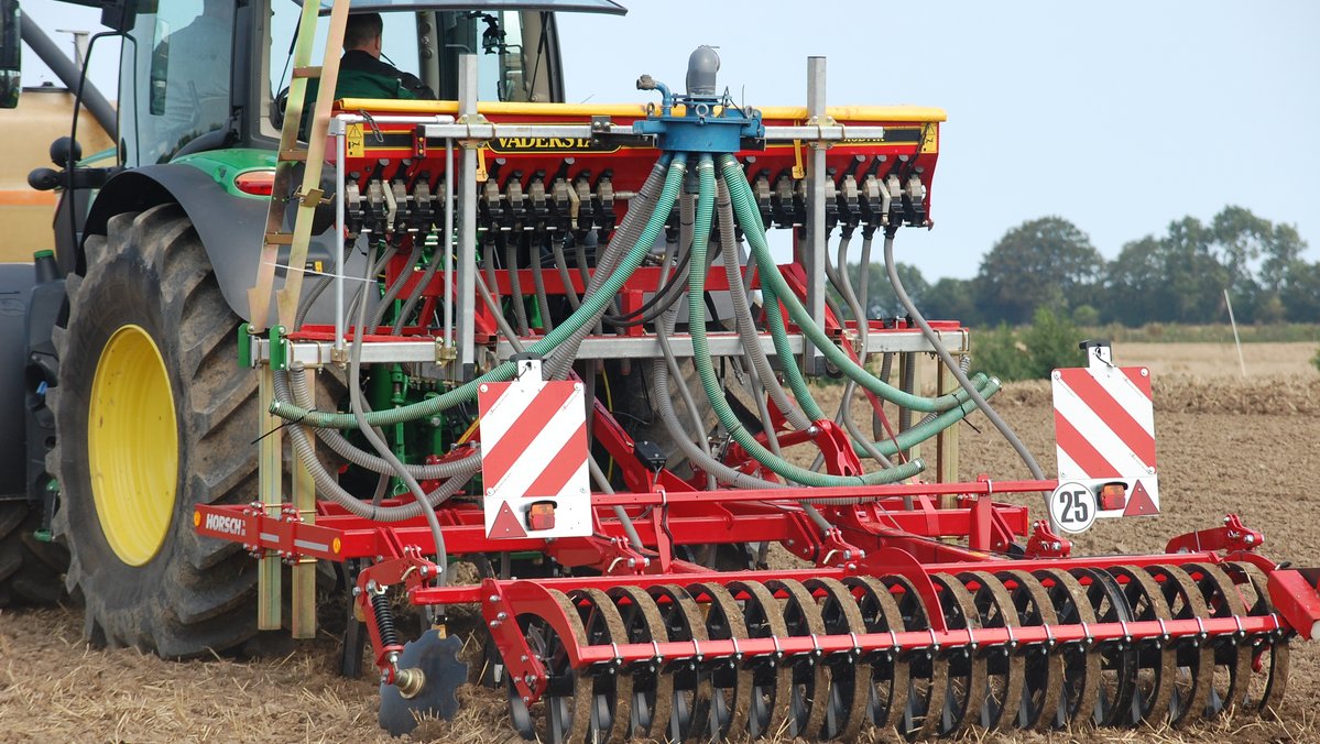 Ein Traktor fährt mit einer Sämaschine auf einem Acker.