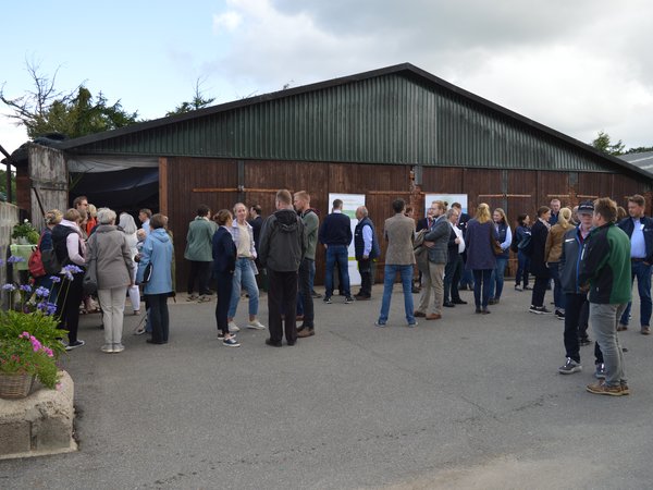 Eine Gruppe von Menschen steht vor einer Halle auf einem Landwirtschaftlichen Betrieb.