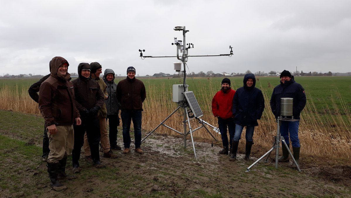 Eine Gruppe von Menschen steht neben einer Wetterstation auf dem Feld.